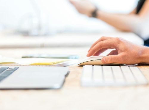 A person working at a laptop with a wireless mouse and keyboard in a bright office setting.